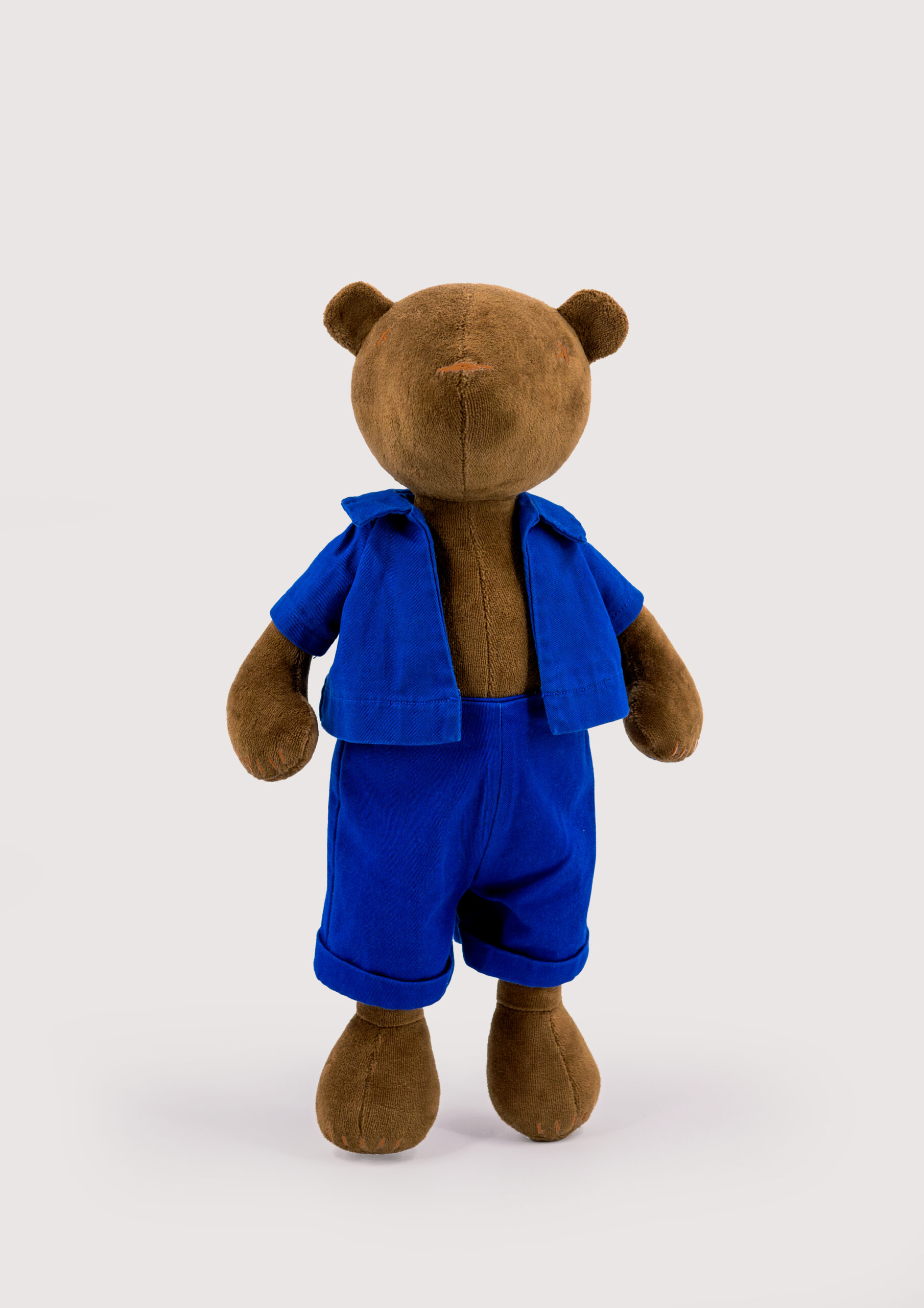 Ours en peluche marron portant une salopette bleue sur fond clair