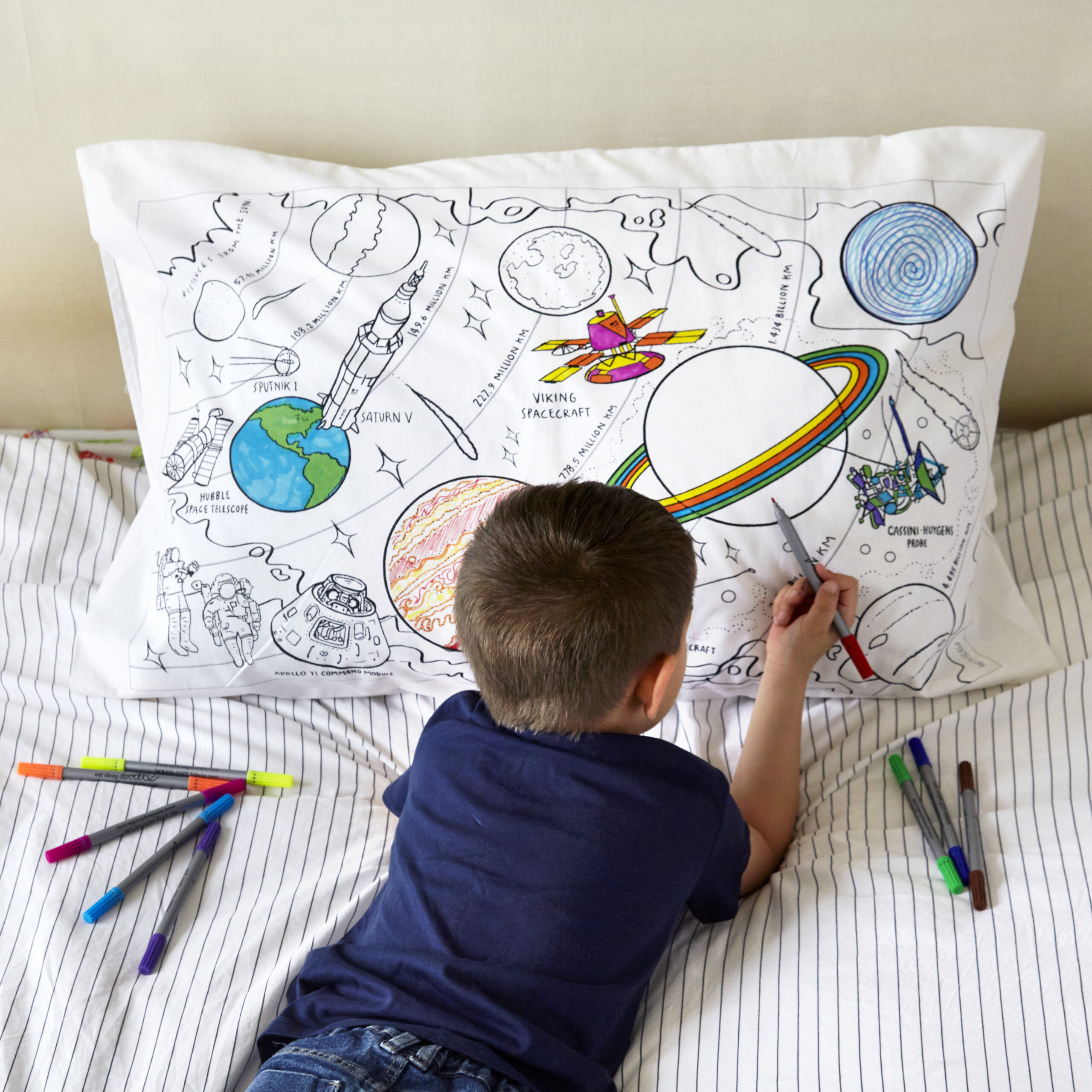 Enfant coloriant une couverture illustrée sur l’espace avec des feutres colorés