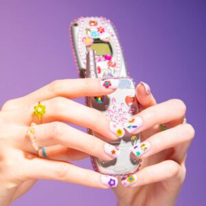 Mains tenant un téléphone à clapet argenté décoré de strass et d’autocollants colorés
