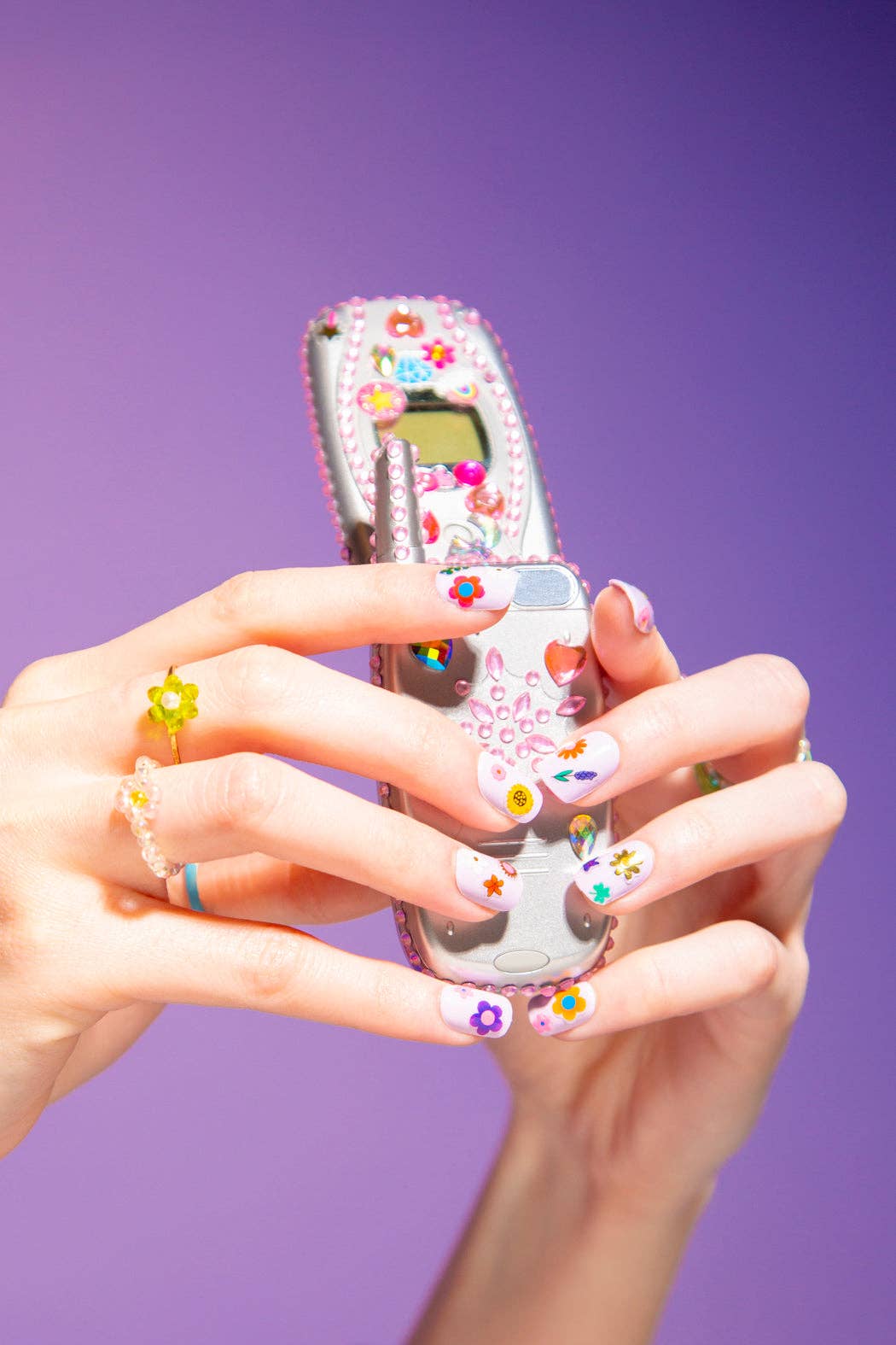 Mains tenant un téléphone à clapet argenté décoré de strass et d’autocollants colorés